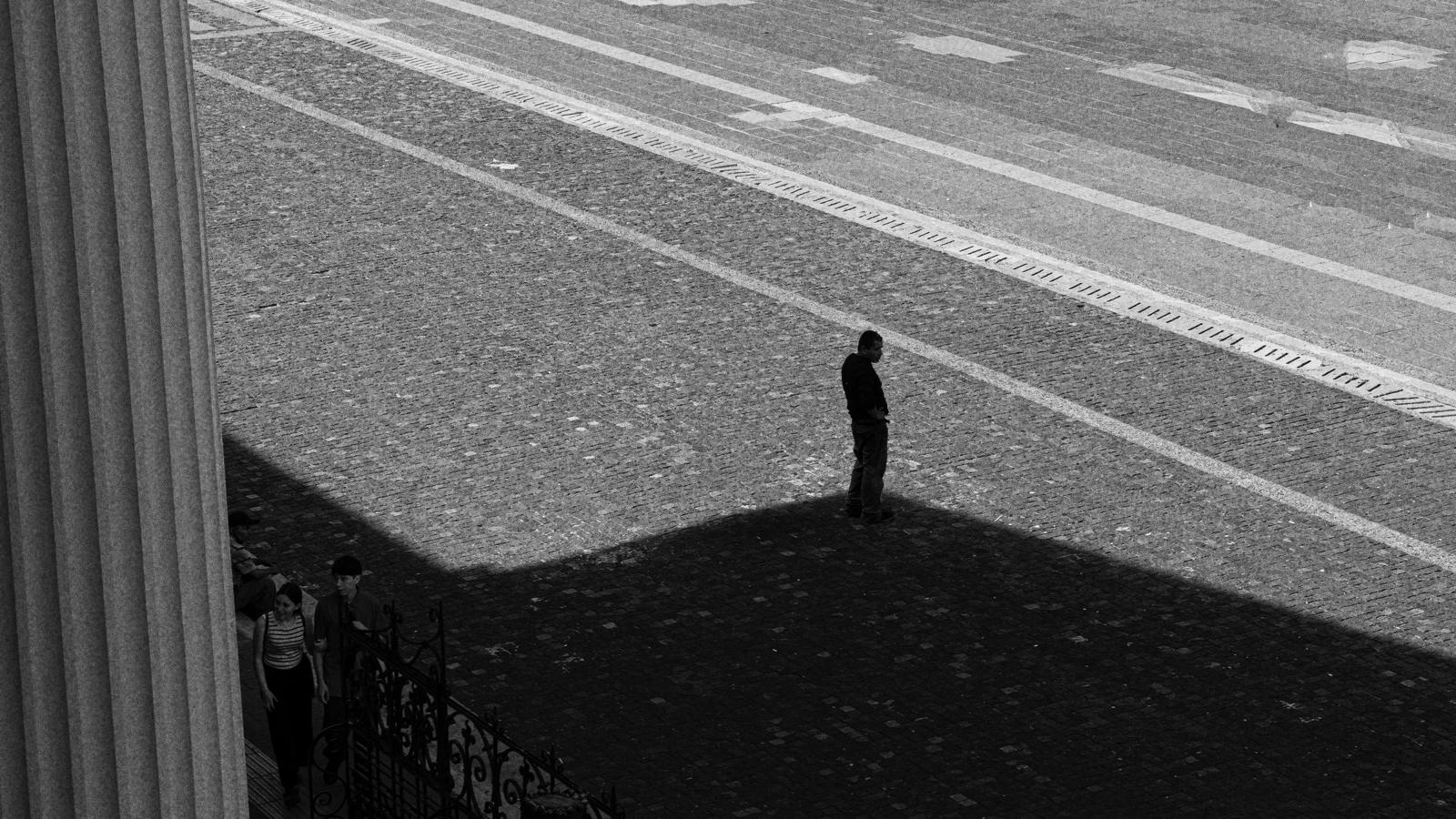 Una figura solitaria y su sombra sobre el empedrado de una plaza